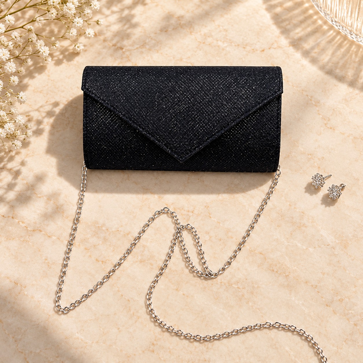 Black shimmer envelope clutch with silver chain on warm stone
